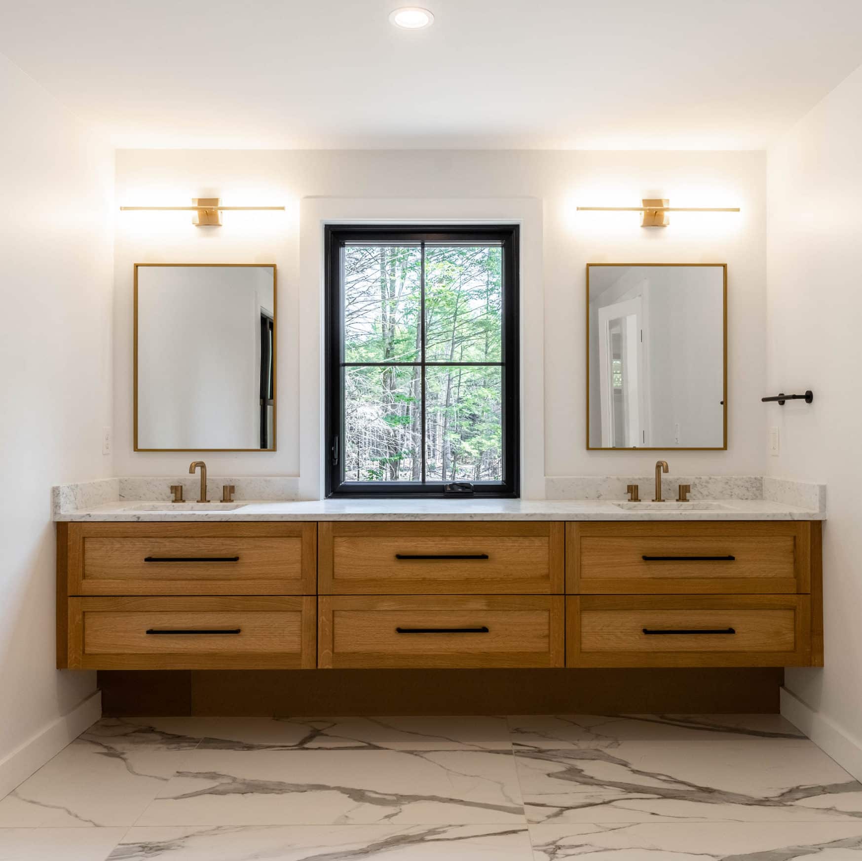 Bathroom with a floating walnut dual vanity. Each sink has a rectangular mirror above it, and there is a window between the mirrors. The floor resembles veined marble.