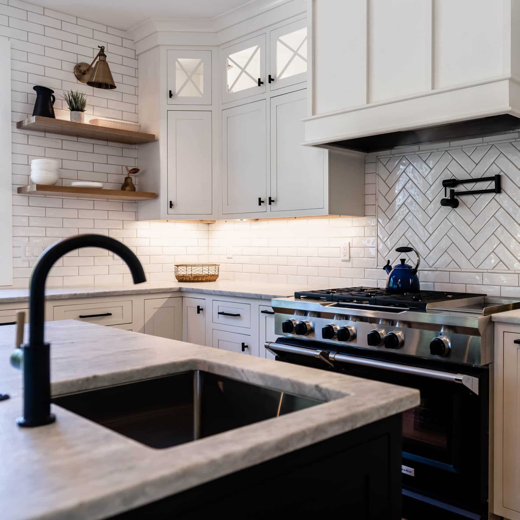 Corner of a kitchen. The cabinets are white with black hardware, and set against subway tile in both standard and herringbone patterns.