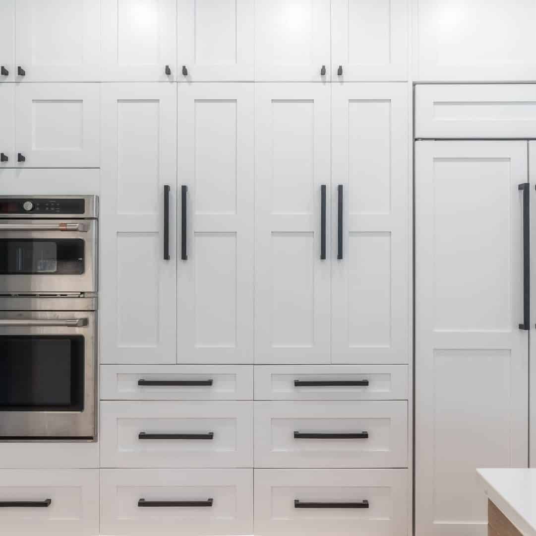 White pantry wall with long black cabinet handles and hidden fridge paneling