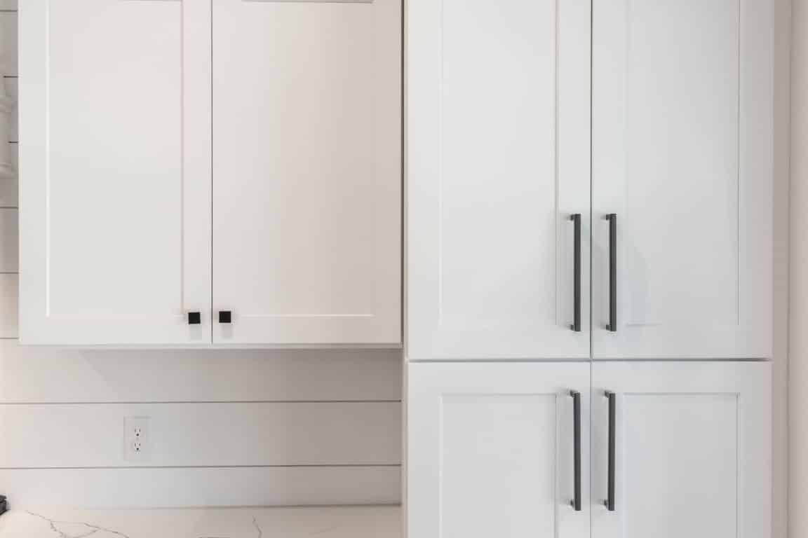 A set of frameless white Shaker cabinets with black hardware in front of a white shiplap wall.