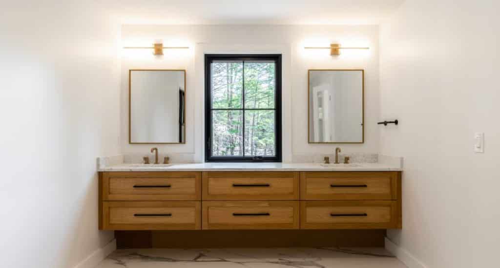 A floating wooden vanity stained in a rich walnut. The vanity has dual sinks, each with a gold-rimmed mirror above.