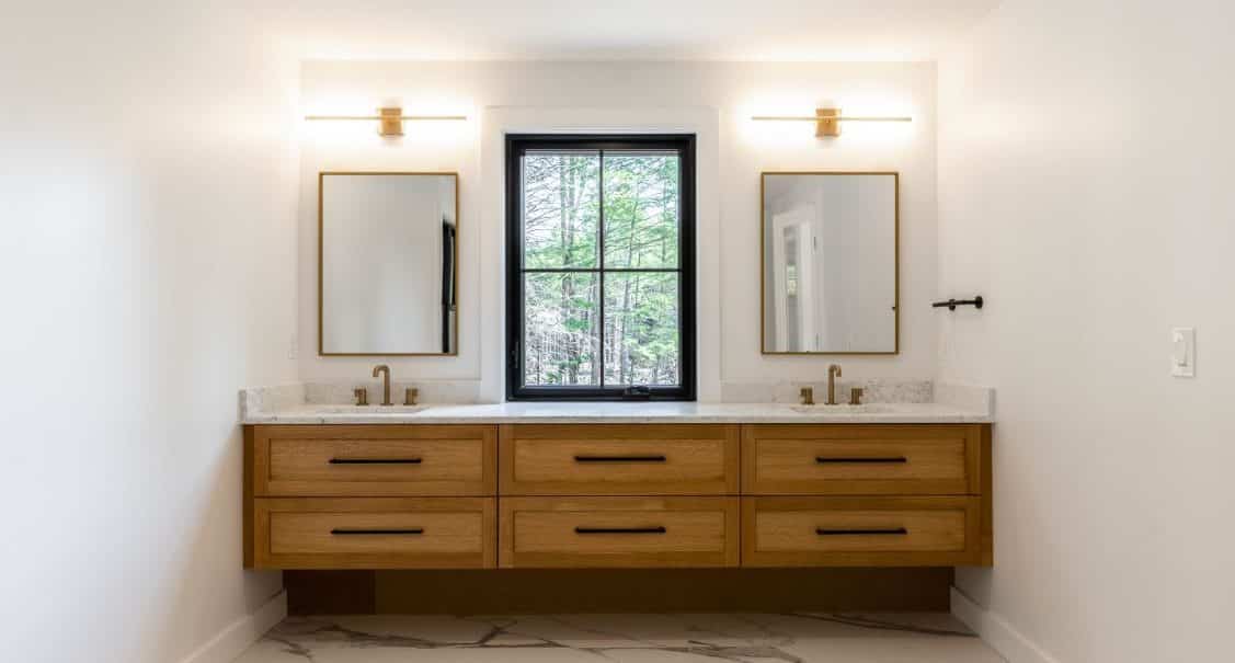 A floating wooden vanity stained in a rich walnut. The vanity has dual sinks, each with a gold-rimmed mirror above.