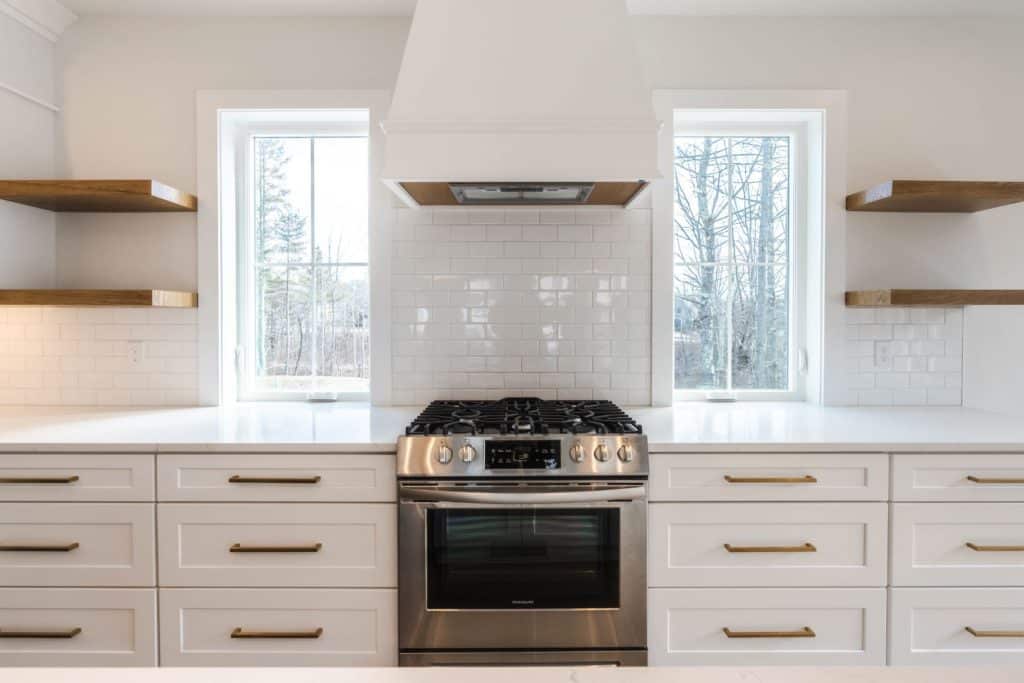 Bright kitchen with white subway tiles, a white range hood, brightly polished stove, and floating wooden shelves