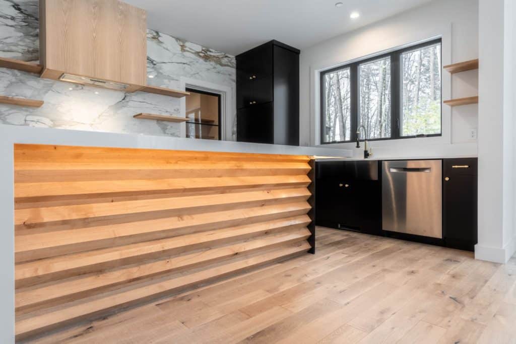 Close focus on a custom kitchen island. One side of the island is natural wood, built to look like the folds of an accordion fan. The top of the island is quartz in a half-waterfall shape.