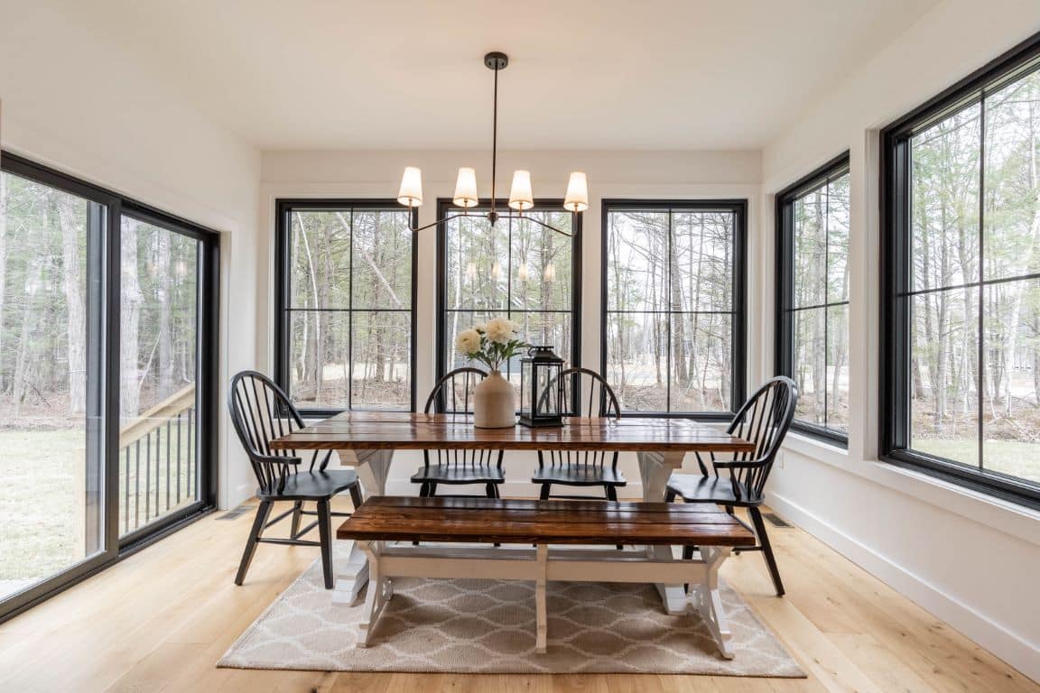 A dining table in a shiny lacquered wood sits in a breakfast nook. It's surrounded by large windows on two sides, and a sliding glass door leading out to the yard on the third.