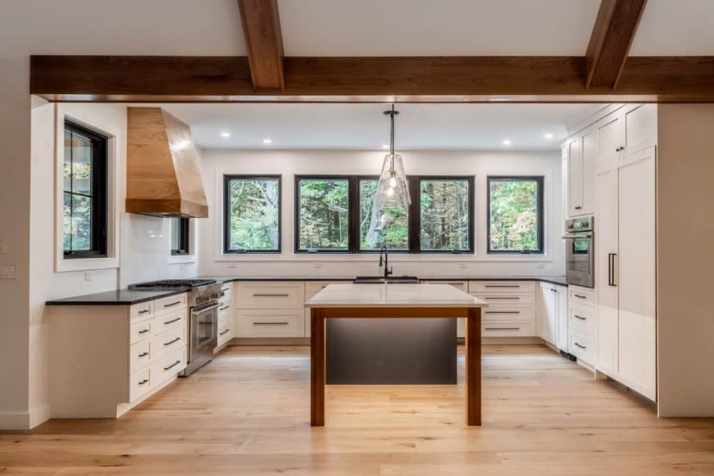 A brightly lit kitchen uses bold black and wooden accents to great affect. The wooden accents in the room - on the kitchen island, range hood, and flooring - reflect the exposed beams of the cathedral ceiling.