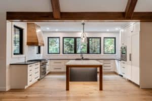 A brightly lit kitchen uses bold black and wooden accents to great affect. The wooden accents in the room - on the kitchen island, range hood, and flooring - reflect the exposed beams of the cathedral ceiling.