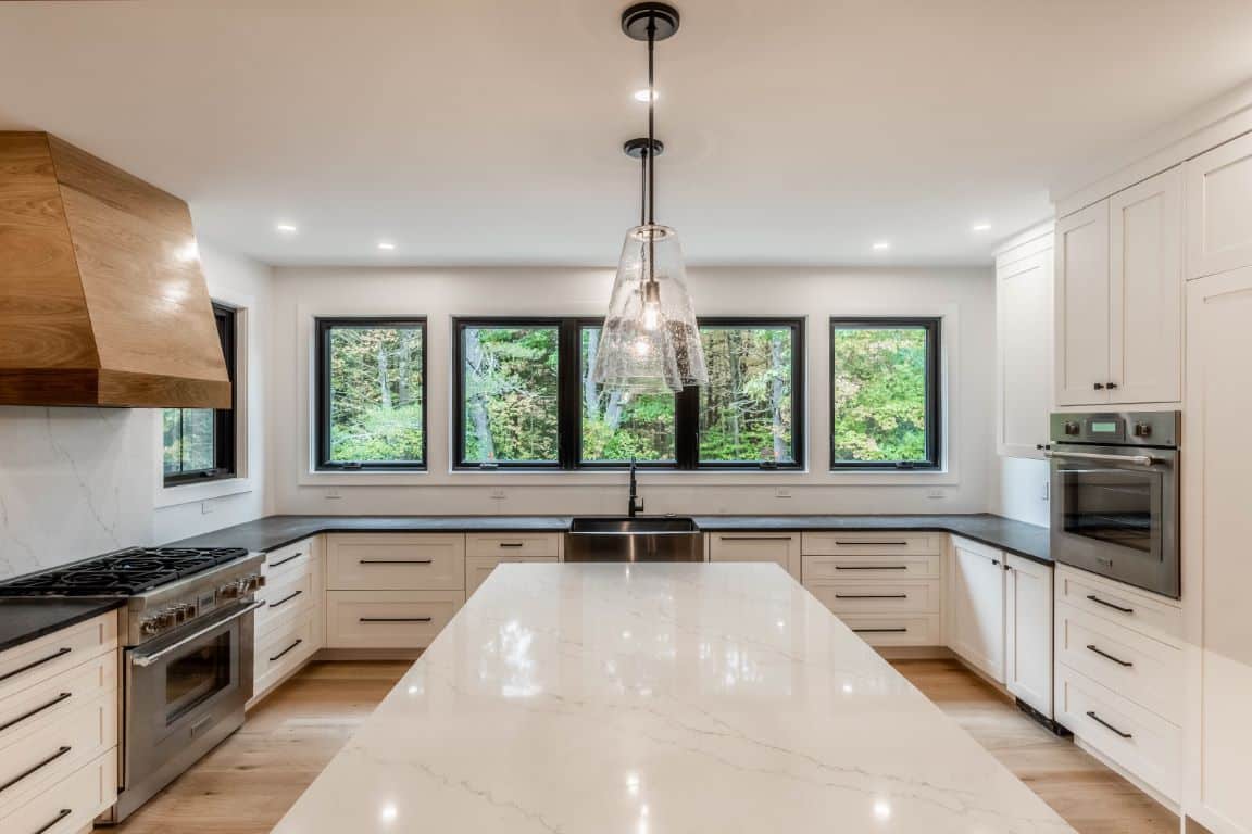 Bright white kitchen with six windows, hanging pendant lights over a kitchen island topped with white marble