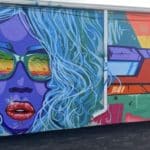 Brightly colored graffiti including a woman's face. Her hair is floating around her face and she is wearing sunglasses.